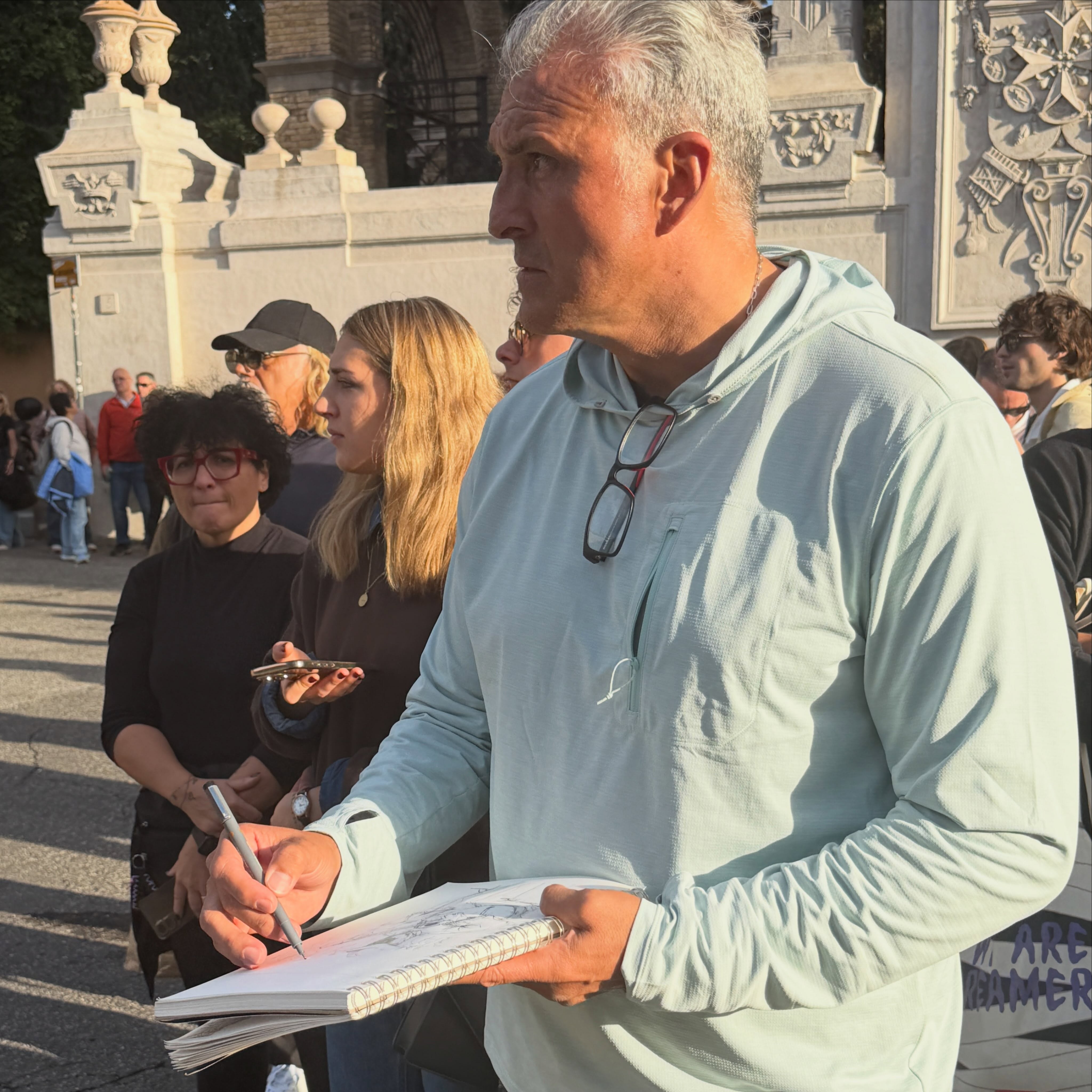 Sometimes the unexpected moments become some of the best memories. ❤️

Yesterday, Fred and I stood in line for 90 minutes to peek through the famous keyhole in Rome that perfectly frames the dome of St. Peter’s Basilica.

While we waited, a gentleman entertained the crowd with his guitar, singing in both English and Italian. We recognized about half the songs, and it certainly made the wait more enjoyable!

Fred decided to pull out his sketchbook and draw the musician.

A few minutes later, I noticed a woman to my right peeking over my shoulder to see what Fred was doing. I mentioned it to him and stepped aside so she could get a better look.

Before I knew it, eight or nine people had gathered behind us, watching him sketch!

They complimented his work, took photos and videos, and some even asked for a picture of the drawing itself.

Fred knew he had an audience but just kept right on sketching. Even a couple of young boys wandered over to see what all the excitement was about.

Thankfully, I was able to step ahead and capture a few photos of my own.

There we were, waiting to see one of Rome’s famous views, listening to one artist share his gift through music while another quietly shared his through a sketchbook.

And somehow, both ended up entertaining the crowd.

I think I enjoyed watching all of this unfold as much as anything else we saw that day. ❤️

One of those little travel moments I’ll remember for a long time.

#italy #sketching #joymeter #35thanniversary #rome